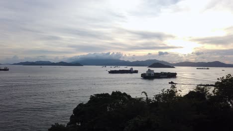 Seeverkehr-In-Der-Bucht-Von-Hongkong-Bei-Sonnenuntergang-Mit-Einem-Großen-Containerschiff,-Das-Vom-Hafen-Wegfährt