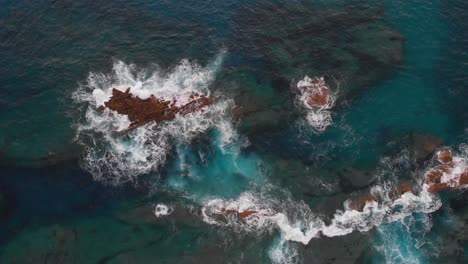 Aerial-top-down-submerged-rocks-waves-breaking-on-translucent-turquoise-water