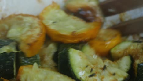 Steaming-close-up-of-oven-roasted-green-and-yellow-courgettes-seasoned-with-thyme,-salt-and-habanero-chili-powder,-gently-stirred-around-with-a-wooden-fork