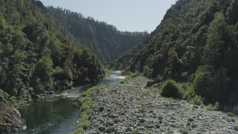Vuelo-Lento-De-Drones-Sobre-Un-Río-Rocoso-Rodeado-De-Un-Bosque-Exuberante