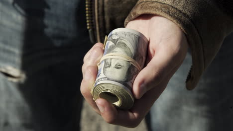 Man-Holds-Big-Roll-of-Money,-Puts-it-Away,-Outside,-Sunny-Day,-Closeup