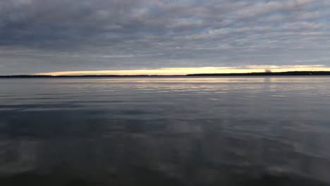 Drone-moving-fast-over-calm-water-on-a-lake-during-sunset