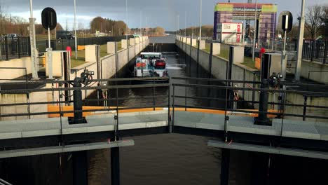 Cargo-ship-entering-Eefde-sluice-gate-with-closing-of-the-doors,-water-ascending-and-continue-on-the-Twentekanaal-on-an-overcast-day-with-a-rainbow-at-the-end