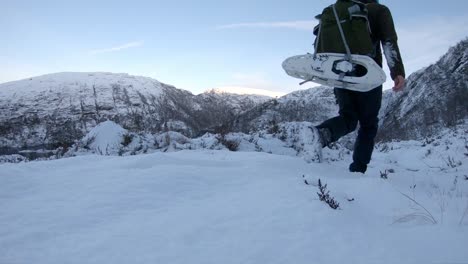 Tired-snowboarder-walking-uphill-with-snowshoes-on-back---Hardangervidda-Norway-Europe