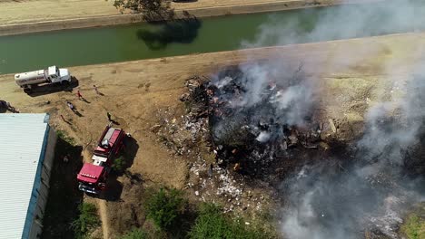 Firefighters-and-firetruck-controlling-a-burnt-down-building-fire-at-a-river,-in-Brazil,-South-America---Aerial-drone-view