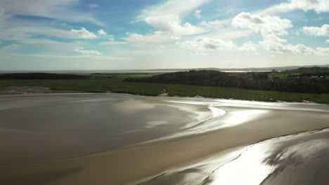 Aerial-view-of-a-beach-at-low-tide-with-the-sun-shimmering-on-the-wet-sand,-bright-sunny-day