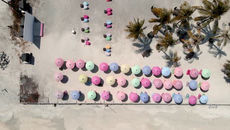 Aerial-top-view-of-ocean-shore,-beach-and-mulitcolored-sunshades-of-hotel-resort-on-Island