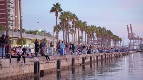 Leute-Sitzen-Am-Wasser-Im-Hafen-Und-Tragen-Gesichtsmasken---Abend-In-Malaga,-Spanien