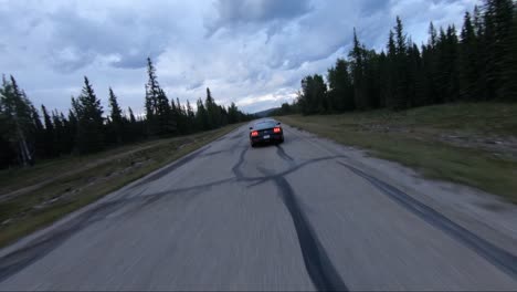 Ein-Dynamischer-Drohnenschuss,-Der-Einen-Ford-Bullitt-Mustang-Verfolgt,-Der-Eine-Leere-Straße-Im-Kanadischen-Hinterland-Hinunterfährt