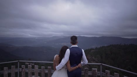 Braut-Und-Bräutigam,-Die-Auf-Die-Berge-Mit-Wolkendecke-In-Zeitlupe-Blicken,-Während-Sie-Sich-Umarmen