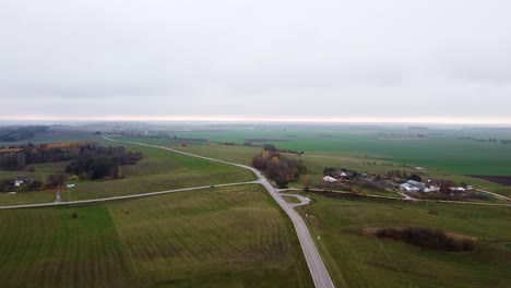 Aerial-top-shot-of-a-small-but-long-country-road-with-green-meadow-surrounding-it