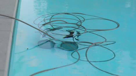Der-Elektrische-Pool-Reinigungsroboter-Reinigt-Den-Pool-Unter-Wasser,-Wobei-Das-Stromkabel-In-Klarem,-Reflektierendem-Wasser-Schwimmt