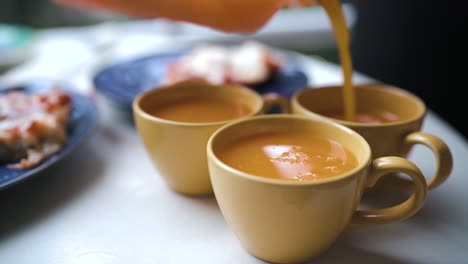 Close-up-of-three-yellow-cups-getting-filled-with-orange-juice-outdoor