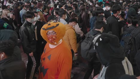 Guy-Wearing-Face-Mask-Partner-In-Pumpkin-Costume-Walking-In-The-Crowd-On-Halloween-Night-In-Shibuya,-Tokyo,-Japan-Amidst-The-Coronavirus-Pandemic
