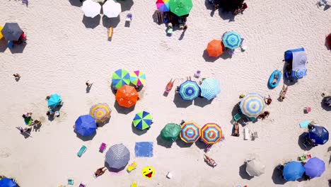 Luftaufnahmen-Von-Oben-Nach-Unten-Von-Menschen-Und-Sonnenschirmen-An-Einem-Weißen-Sandstrand-An-Windigen-Tagen