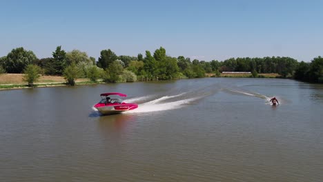 Aerial-view-of-a-boat-and-man-wake-boarding---slow-motion,-pull-back,-drone-shot