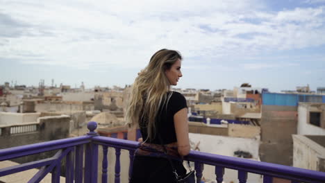 Beautiful-Caucasian-Girl-Standing-And-Leaning-On-Railings-With-City-View-Of-Essaouira,-Morocco