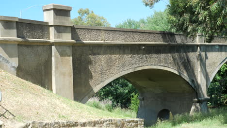 Old-Historic-Cement-Arch-Bridge-Over-River,-PAN-RIGHT