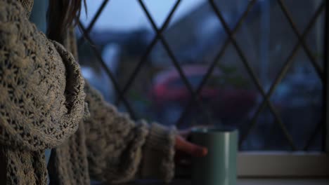 Woman-reaches-for-mug-of-hot-coffee-in-window-medium-shot