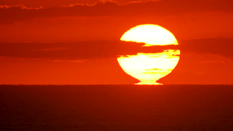 Closeup-of-a-sunrise-as-the-sun-rips-away-from-the-ocean-horizon,-glowing-the-sky-orange-and-pink