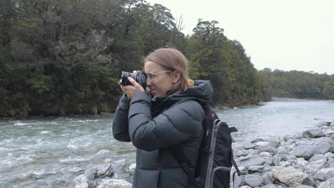 Woman-in-hiking-gear-photographing-a-lake-in-a-valley-on-New-Zealand's-South-Island
