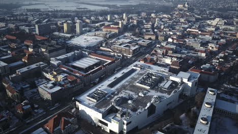 Flying-above-big-shopping-centre-towards-main-intersection-in-Nitra-City,-Winter,-Aerial-shot,-Slovakia