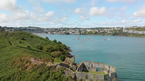 Aerial-video-pans-along-coastline-over-derelict-outpost-to-reveal-small-fishing-boat-approaching-and-beautiful-tourist-village-of-Kinsale-in-Background