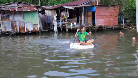 Zwei-Kinder-In-Bangkok,-Die-Vor-Ihren-Häusern-Im-Wasser-Spielen-Und-Das-Beste-Aus-Ihrer-Armut-Machen