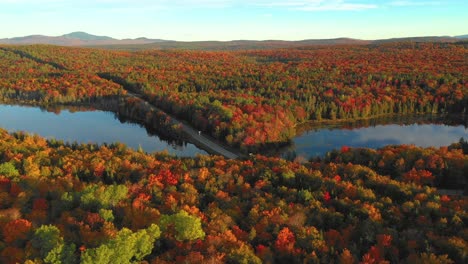 Aerial-footage-sliding-right-across-a-forest-in-autumn-colors-with-two-reflective-ponds