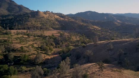 Train-in-distance-passing-by-mountain-landscape-in-Tehachapi,-California,-AERIAL