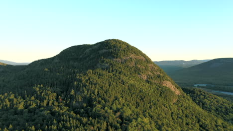 Aerial-drone-shot-rising-up-to-the-peak-of-Bore-Mountain-over-thick-green-forest-trees-and-lakes-of-the-Maine-wilderness