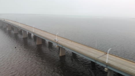 Aerial-shot-of-cars-and-trucks-move-across-a-multilane-long-raised-bridge-over-a-massive-area-of-water