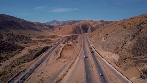 Cars-and-semi-trucks-driving-on-Mojave-Desert-highway-in-California,-AERIAL-PULL