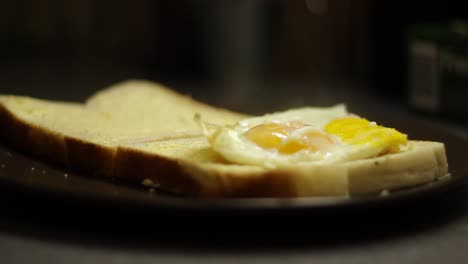 Fried-eggs-being-placed-on-a-slice-of-white-bread,-still-steaming