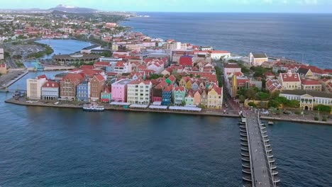 Willemstad-in-Curacao,-aerial-dolly-shot-of-waterfront-with-colorful-historic-buildings-and-Queen-Emma-bridge