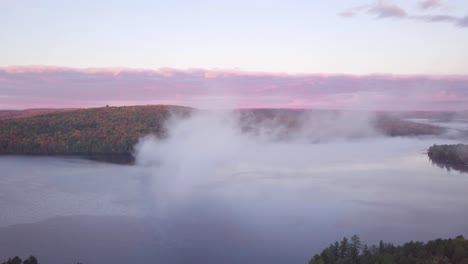 Aerial-Sunrise-Wide-Shot-Flying-Through-Cloud-Fog-Showing-Misty-Lake-And-Pink-Clouds-And-Fall-Forest-Colors-in-Kawarthas-Ontario-Canada