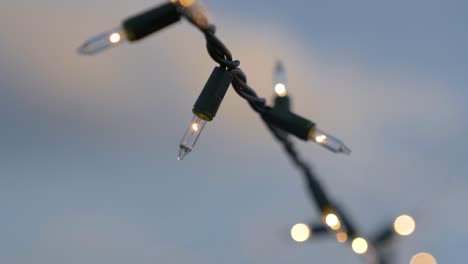 Close-up-of-Christmas-lights-strung-outside-in-the-summer-during-dusk