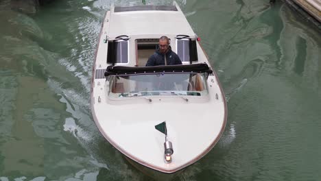 Man-steer-luxury-motorboat-on-Venice-canal-tide-water-way-between-old-building-and-several-gondolas