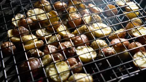 Flipping-browned-herbed-new-potatoes-in-a-wire-basket-on-a-hot-grill-with-red-embers-glowing-beneath