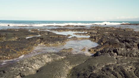 Small-waves-coming-towards-the-camera-covering-a-lava-rock-formation