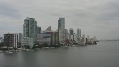 Aerial-shot-rising-from-the-water-showcasing-buildings-in-downtown-Miami-along-the-bayside