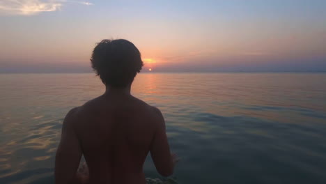 Man-walks-at-sunset-through-the-calm-sea-towards-fading-the-sun-on-the-horizon