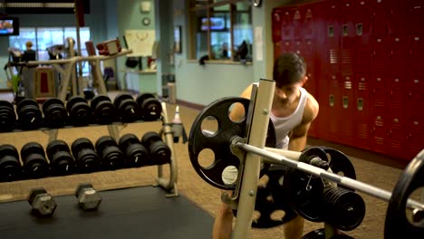 Teen-boy-bodybuilder-putting-a-two-large-weights-onto-a-barbell-in-a-fitness-gym