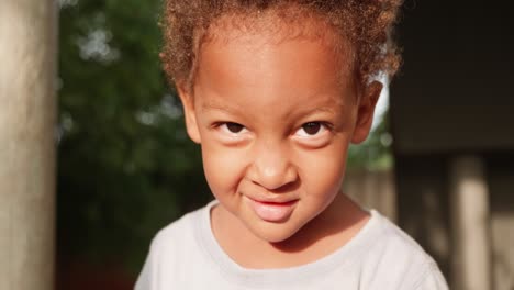 A-close-up-shot-of-a-young-mixed-raced-child's-face-as-he-smirks-and-smiles-into-the-camera