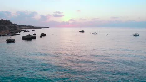 Rising-aerial-shot-over-the-water-at-Konnos-bay-during-sunset-with-pink-glow