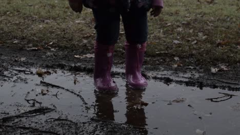 Baby-girl-jumping-with-the-waterproof-pink-boots-on-the-puddle-Bambina-salta-con-gli-stivaletti-rosa-impermeabili-nella-pozzanghera