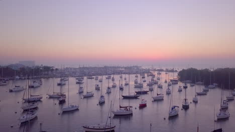 Aerial-fly-over-boat-filled-harbor-towards-pink-sunrise