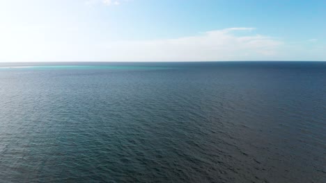 drone-aerial-over-dark-ocean-water-under-blue-sky-and-white-clouds