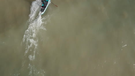 Birds-eye-view-of-a-young-man-stand-up-paddle-boarding-in-the-sea