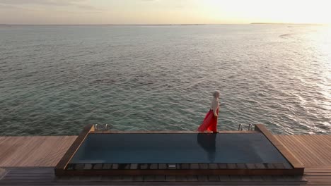 Woman-walks-on-the-edge-of-large-infinity-pool-at-sunset-at-luxury-tropical-resort